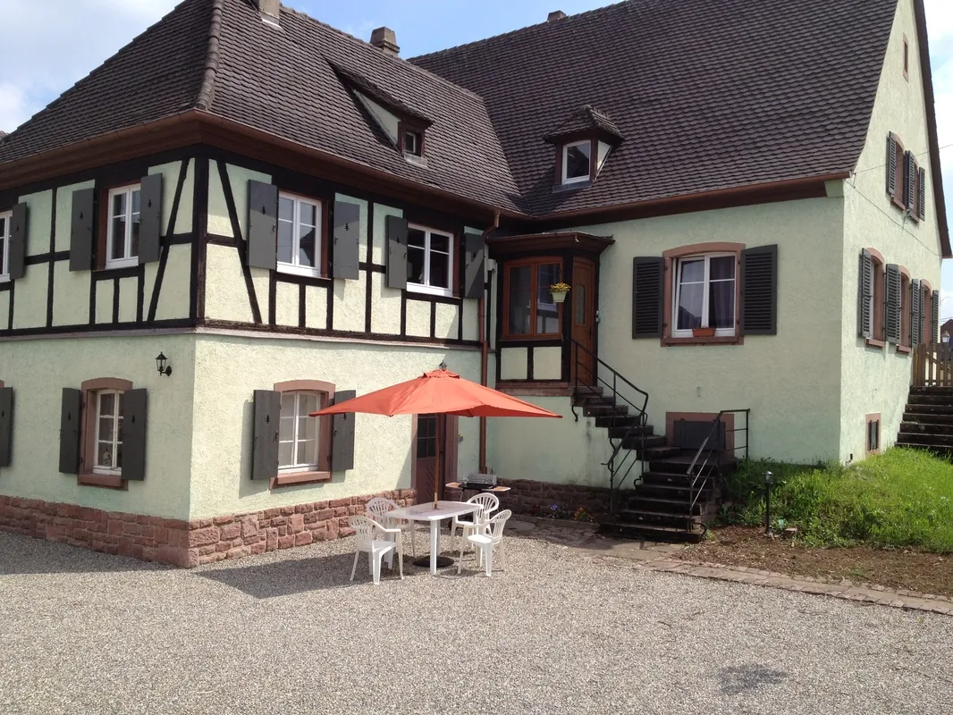 La maison à colombages du gîte Les Érables, avec sa cour et son parasol, un jour d'été